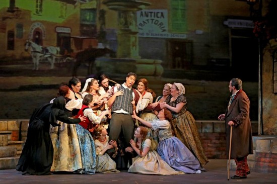 Nemorino surrounded by the women's chorus; Dulcamara (R) looks on in disbelief
